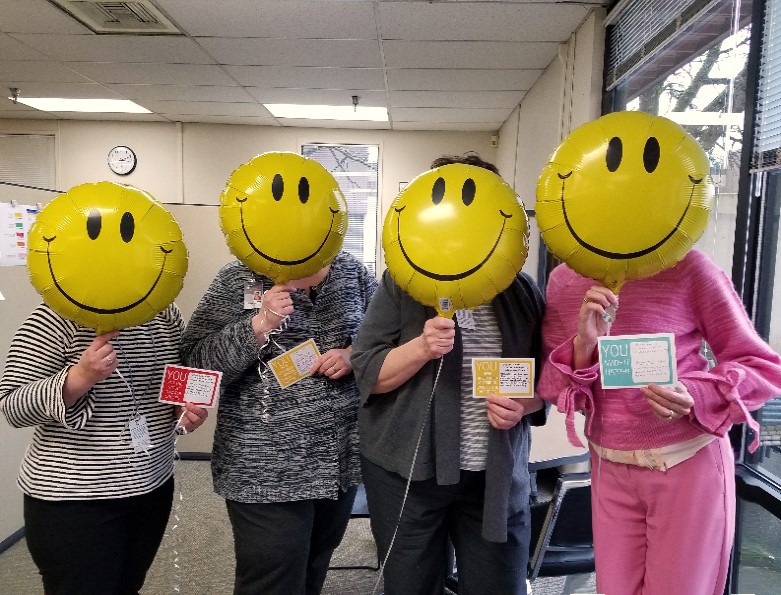 four people standing with smiley face balloons covering their faces