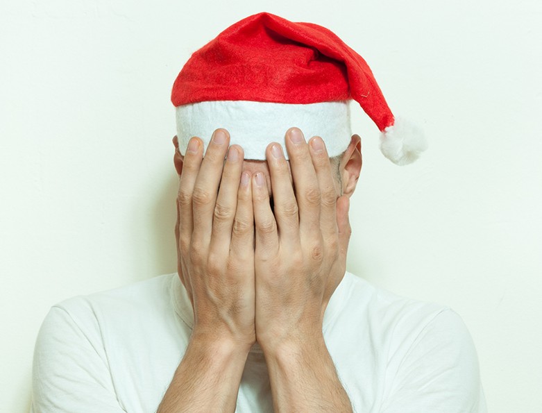 Young man with Santa Claus hat cover his face with his hands feeling lonely and sad for New Year and Christmas holiday depression concept